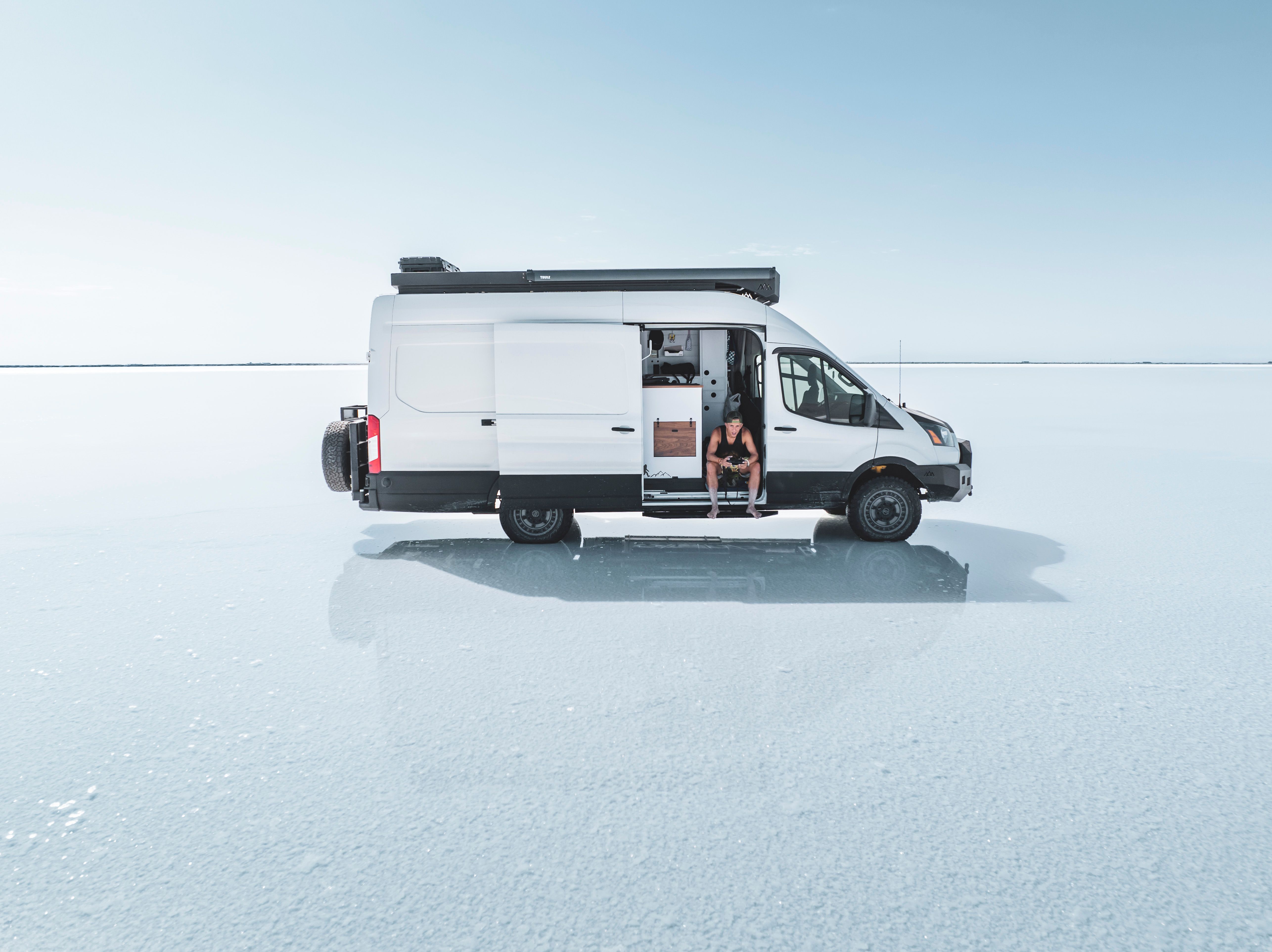 Minimalist photo of a camper van parked on a vast, open salt flat under a clear sky.