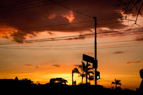 Free Power lines silhouetted against a vibrant sunset sky creating a dramatic urban landscape. Stock Photo