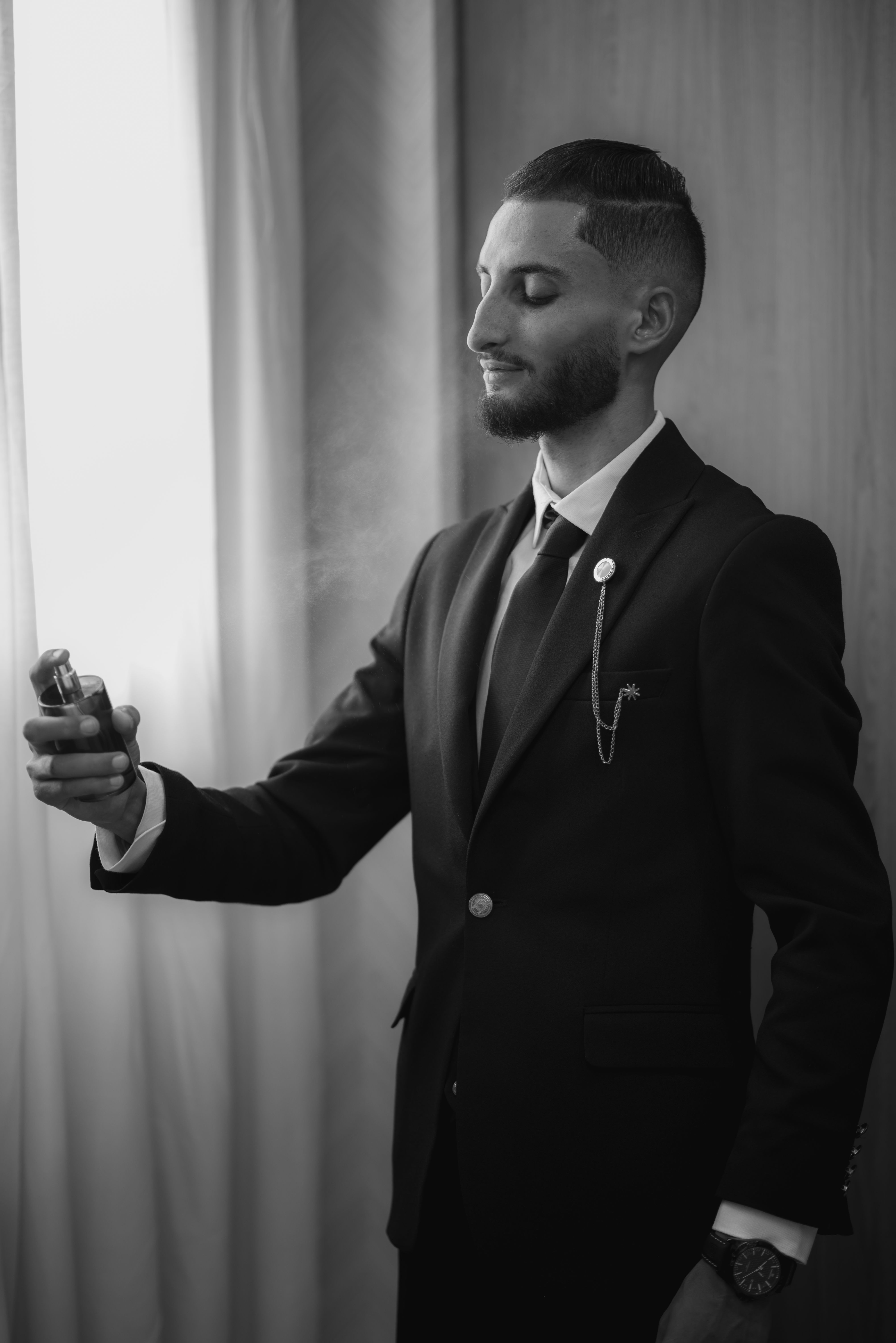 Man in formal suit spraying men's cologne beside a sunlit window, Father's Day fragrance gift