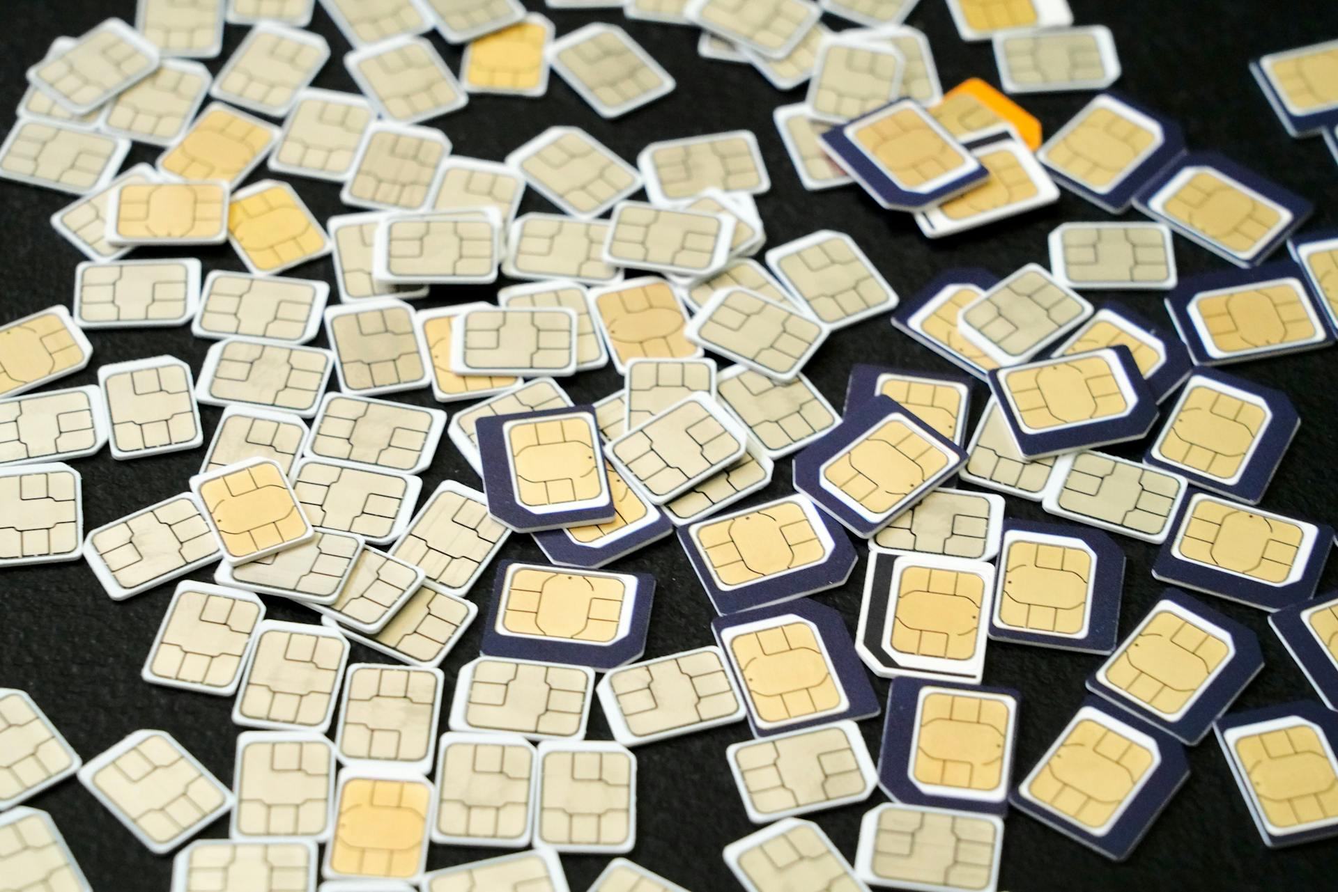 Pile of SIM Cards with Gold Contacts on Black Surface