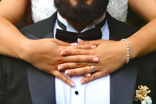 Close-up of a bride embracing a groom, showcasing elegant jewelry and wedding rings.