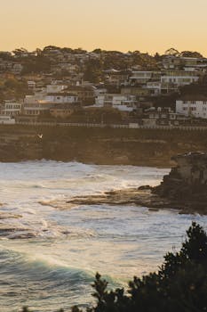 Breathtaking coastal scene at sunrise featuring urban skyline and crashing waves.