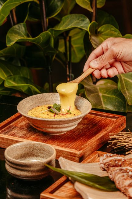 A pot of melted gruyère cheese fondue being stirred with a wooden spoon, with cubed baguette pieces arranged around it for dipping.