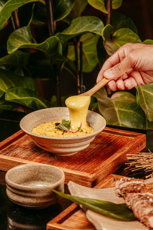 Uma mão mergulha em um fondue de queijo cremoso em uma mesa de jantar rústica.
