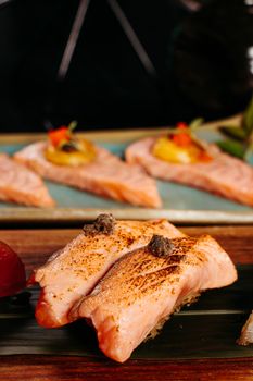 A close-up of delicious grilled salmon pieces with garnish on a wooden platter.