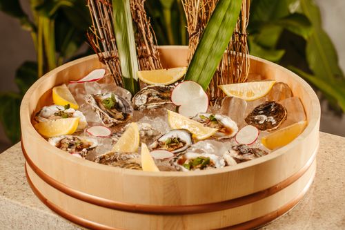 Free A wooden platter filled with fresh oysters, lemon wedges, and garnishes atop ice. Stock Photo