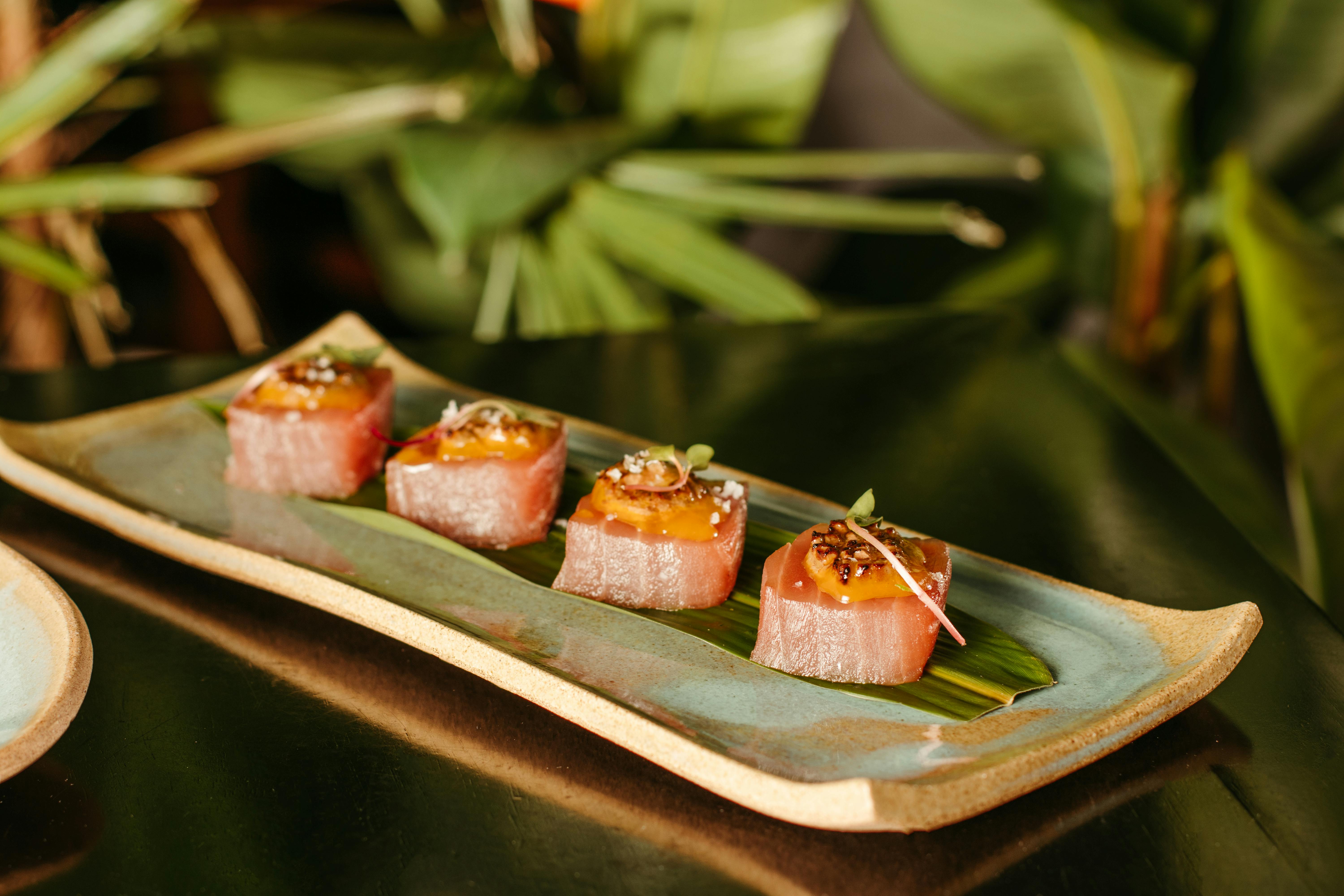 Delicious sushi rolls on a ceramic platter surrounded by lush green leaves.