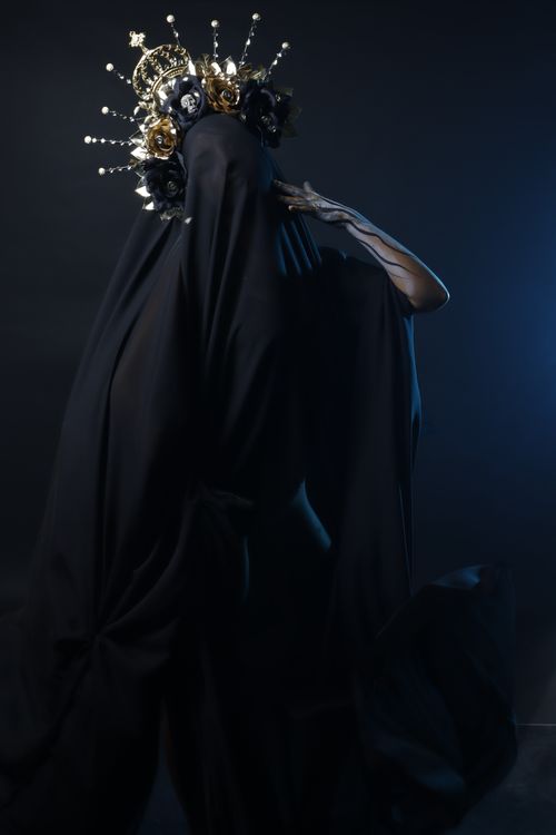 Free A mysterious figure draped in black with an ornate headdress in a dark, moody setting. Stock Photo