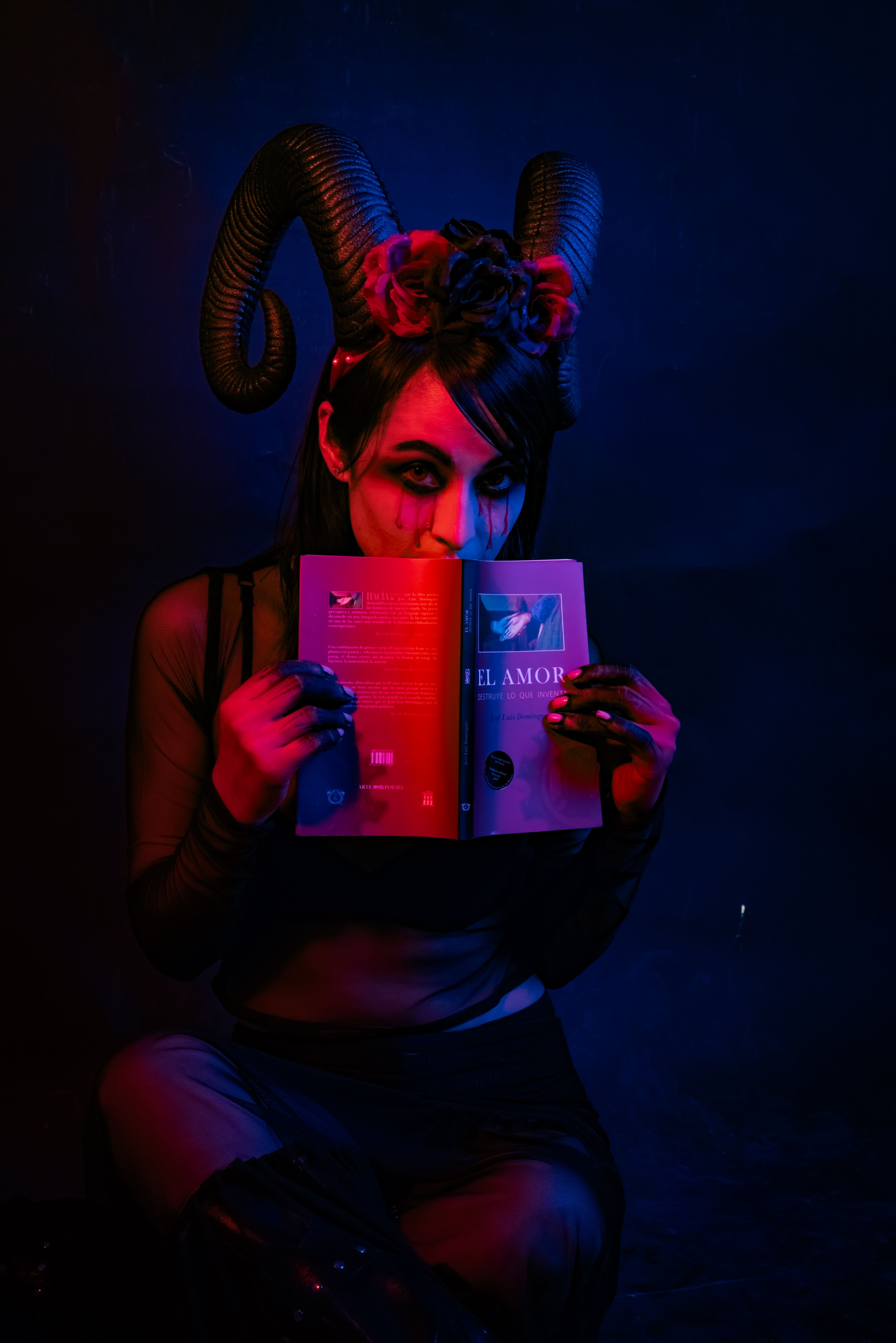 Dark atmospheric portrait of a person with horns reading a book, illuminated by dramatic lighting.