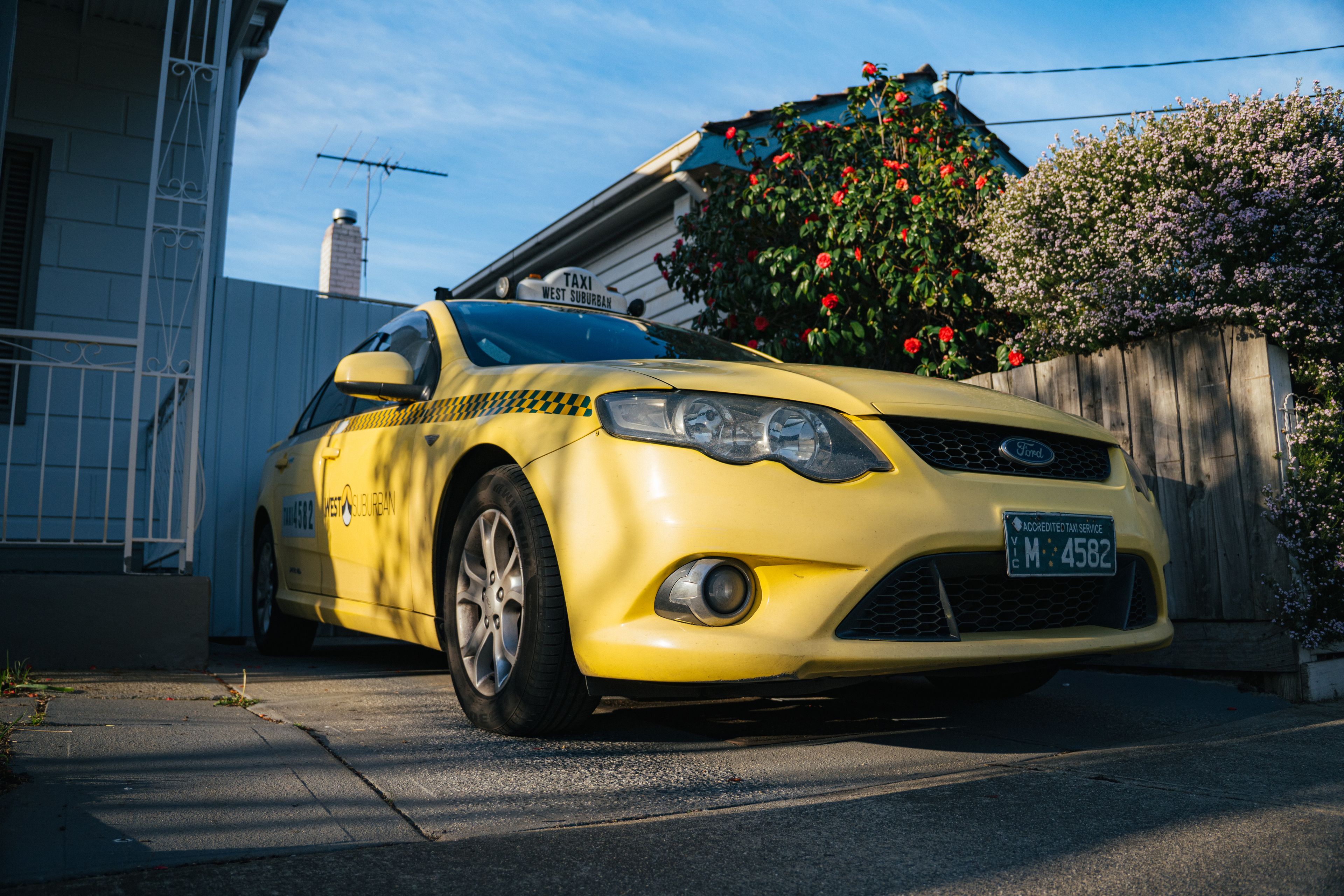 A bright yellow taxi parked in a suburban driveway in Yarraville, showcasing urban lifestyle.