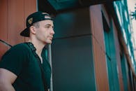 这是一幅轻松的肖像，画中一名男子头戴黑色帽子，身着黑衣，倚靠在建筑物的墙壁上