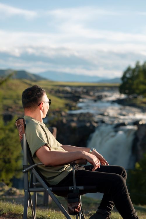 Free A person enjoying a peaceful moment seated by a tranquil waterfall in a natural setting. Stock Photo
