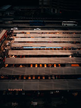 Aerial shot of bustling night market stalls in urban Bangkok, illuminated against the cityscape.