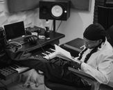 Black and white image of a musician taking a break with a book in a modern recording studio.