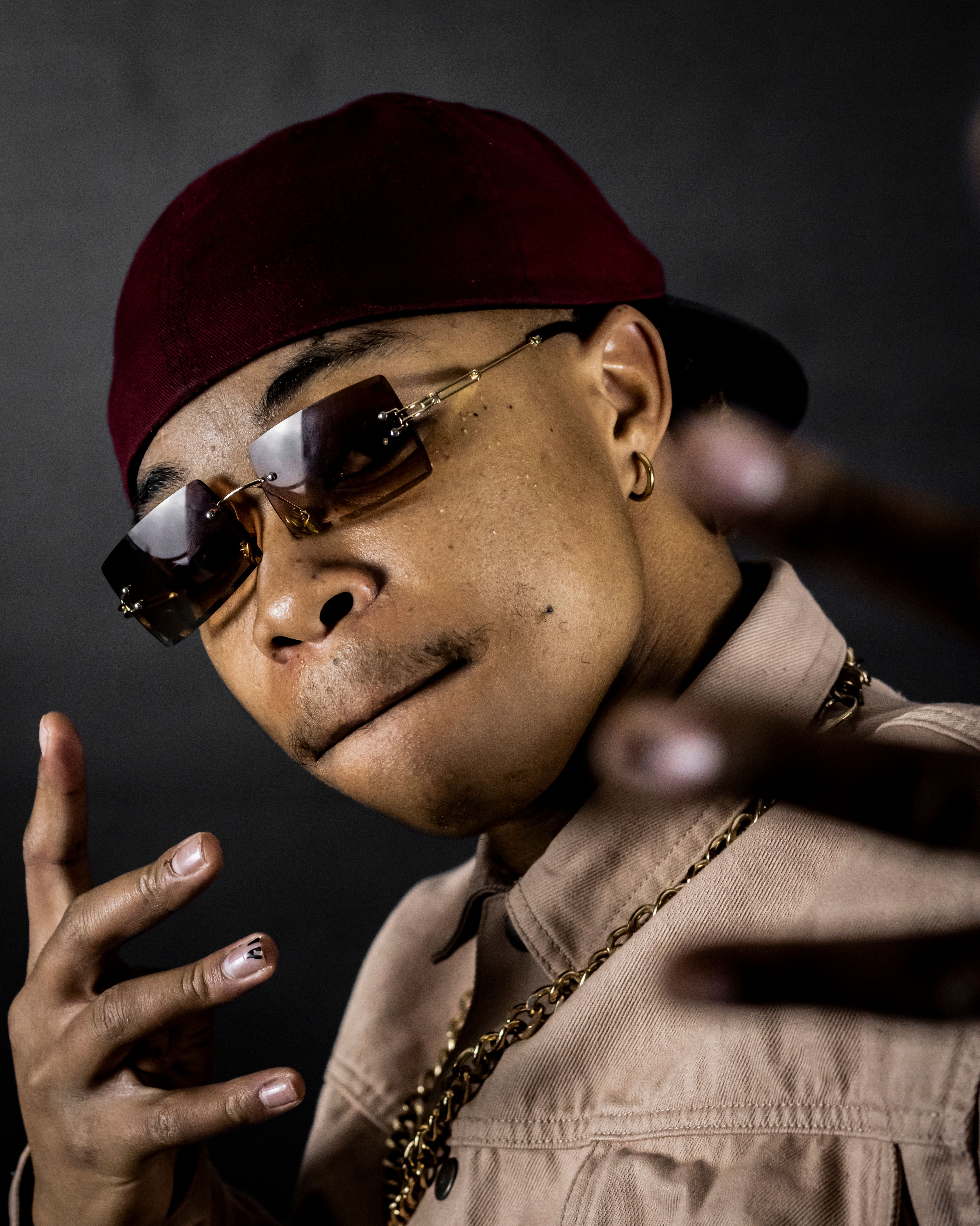 Young adult in sunglasses and cap posing confidently against dark background.