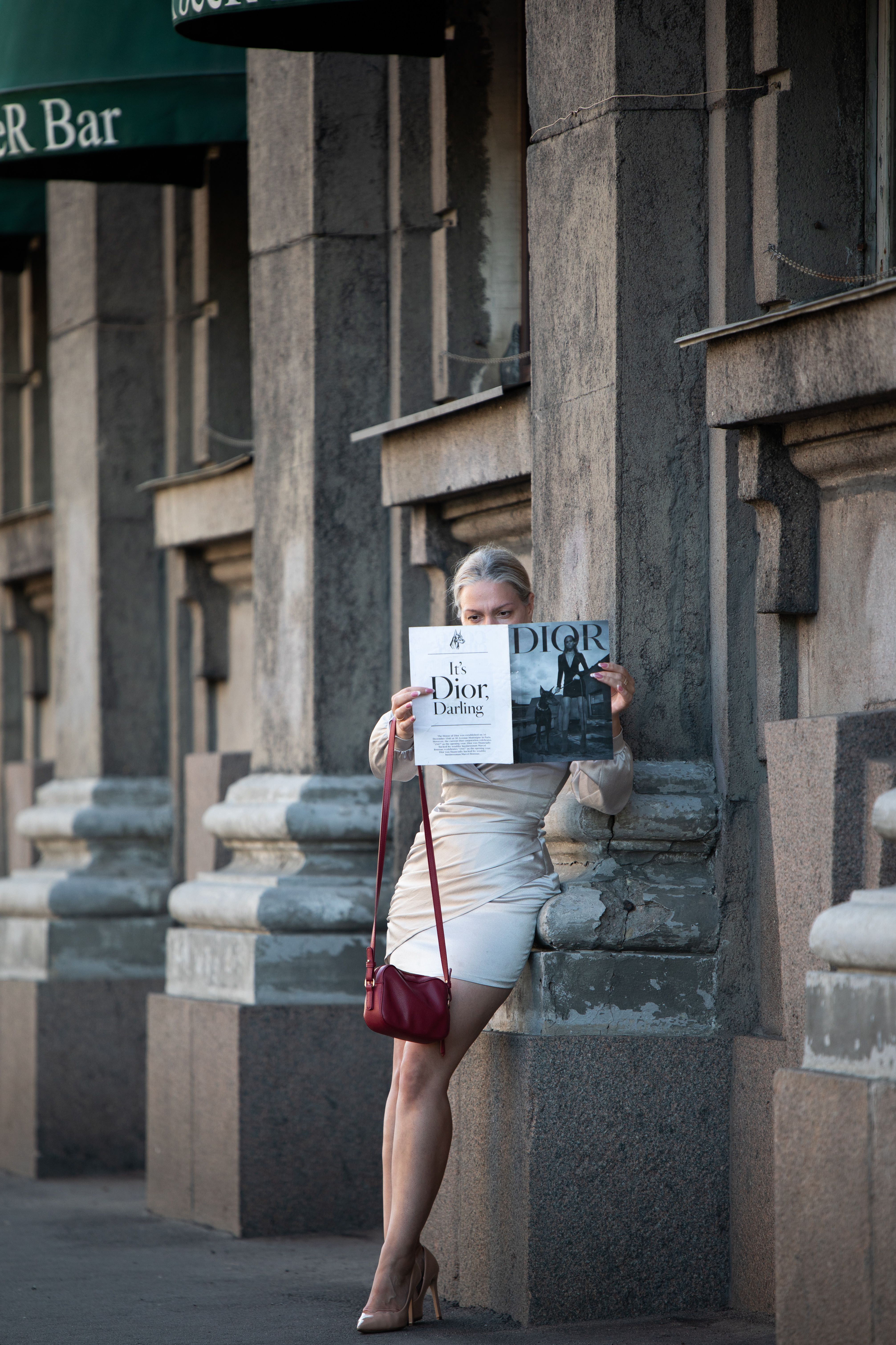 Woman in stylish dress reading a fashion magazine against urban architecture.