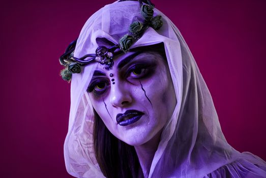 Stunning portrait featuring a woman with halloween makeup and veil against a purple background.