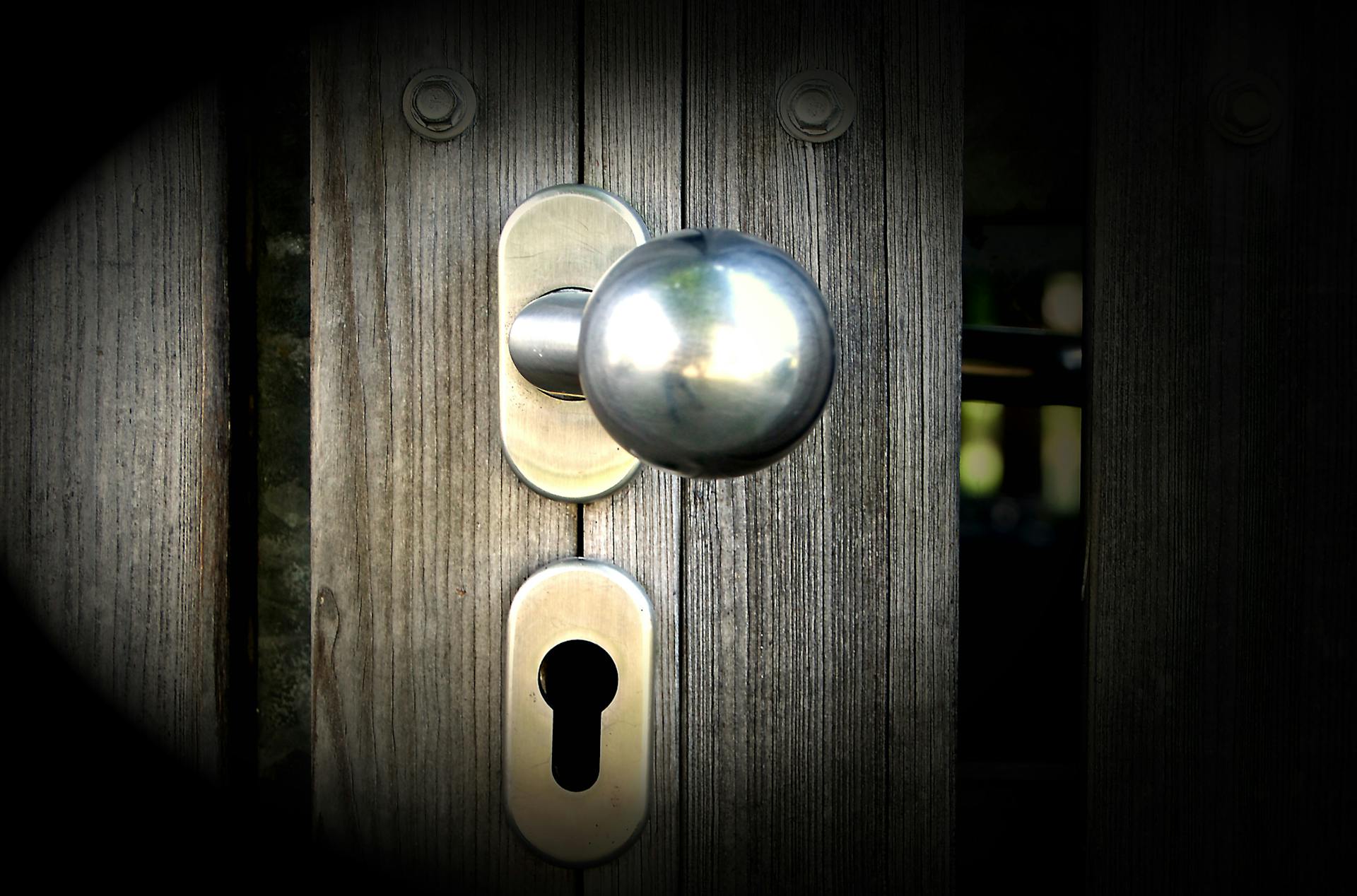 Close-up view of a metal doorknob and keyhole on a wooden gate, emphasizing security and design.