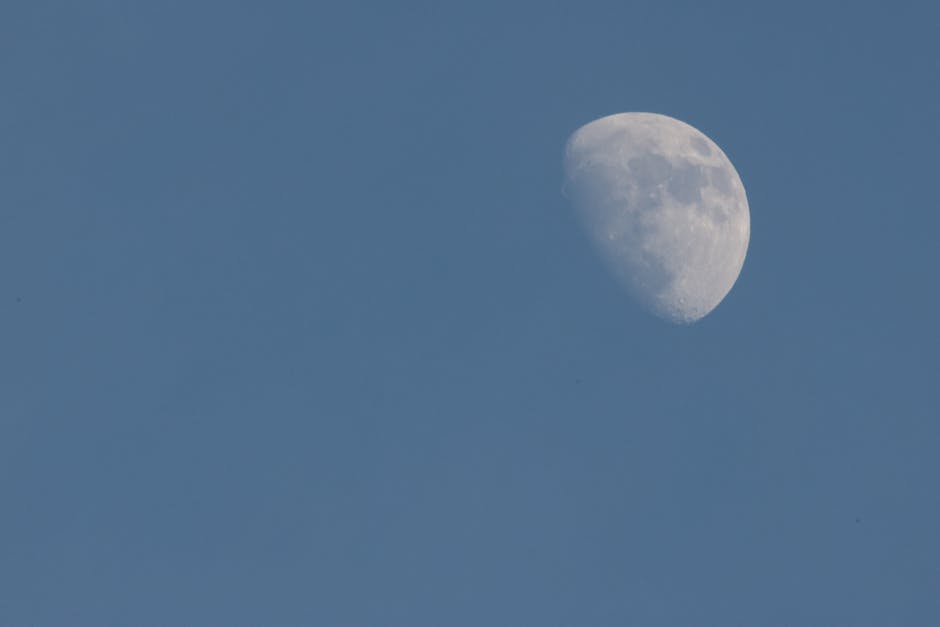 A clear view of the daytime sky featuring a prominent half moon.