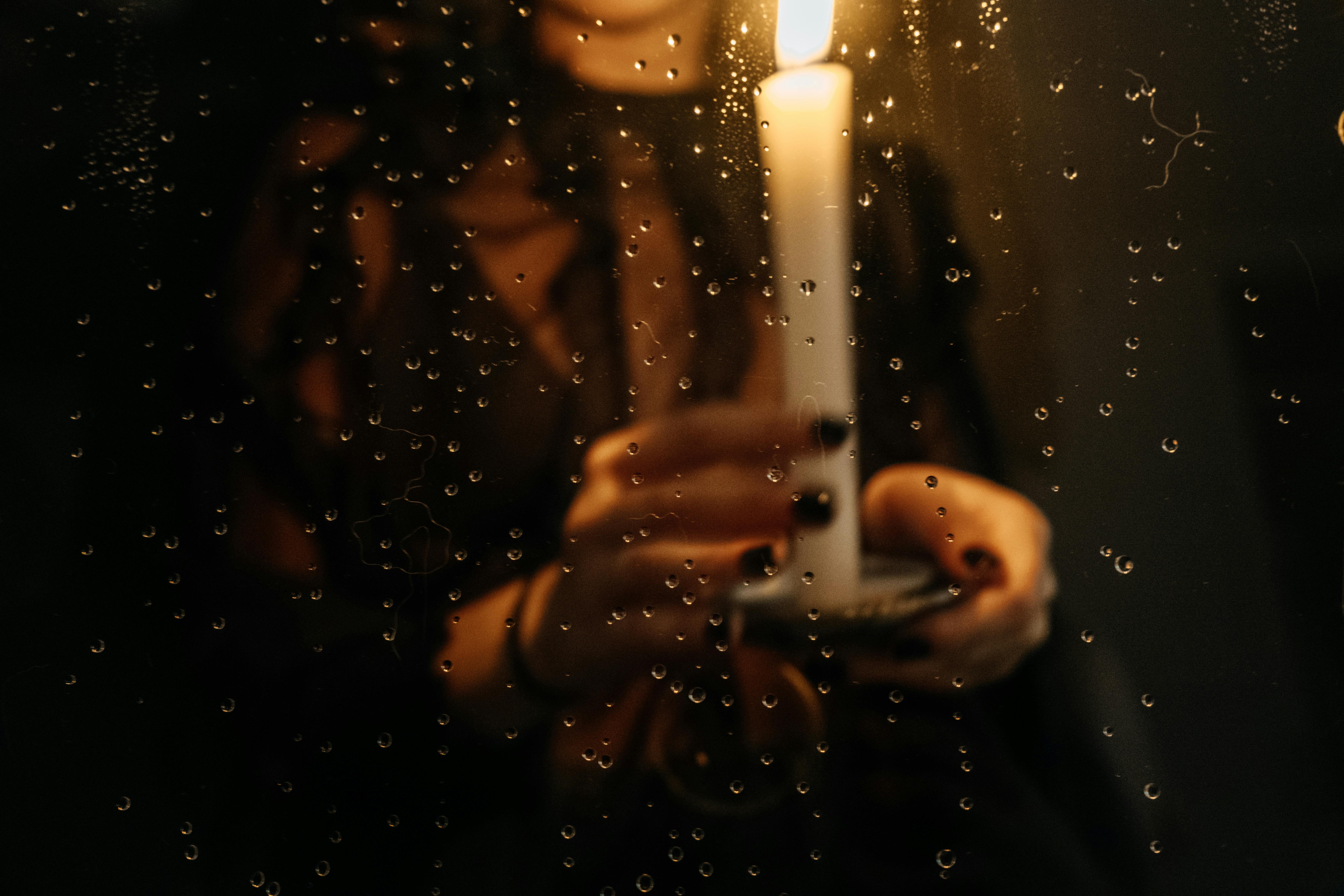 Moody candlelit scene with raindrops on glass window, intimate warm glow inside stormy night