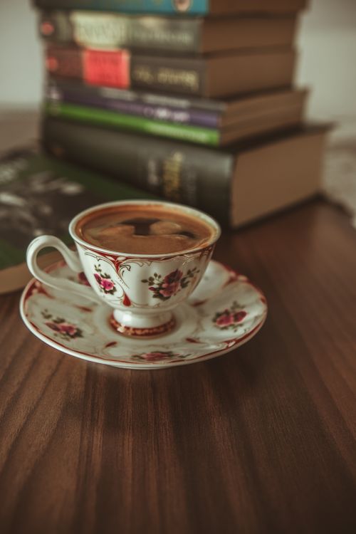 Free Elegant antique teacup filled with coffee beside a stack of books on a wooden table. Stock Photo