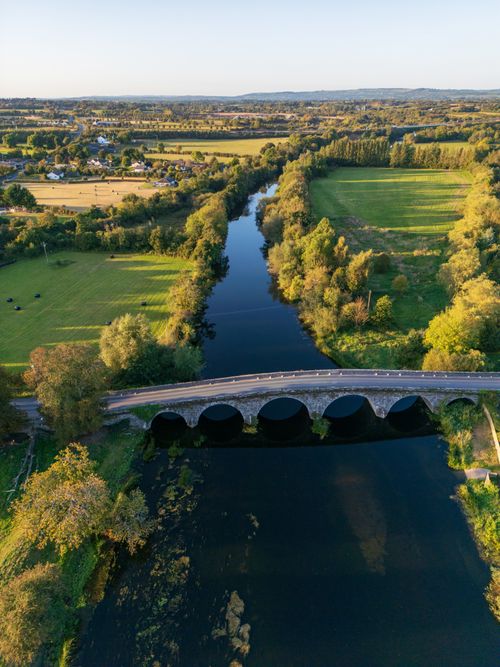 Free Scenic aerial view of Bennettsbridge and River Nore in County Kilkenny, Ireland, featuring lush green landscapes and a stone arch bridge. Stock Photo