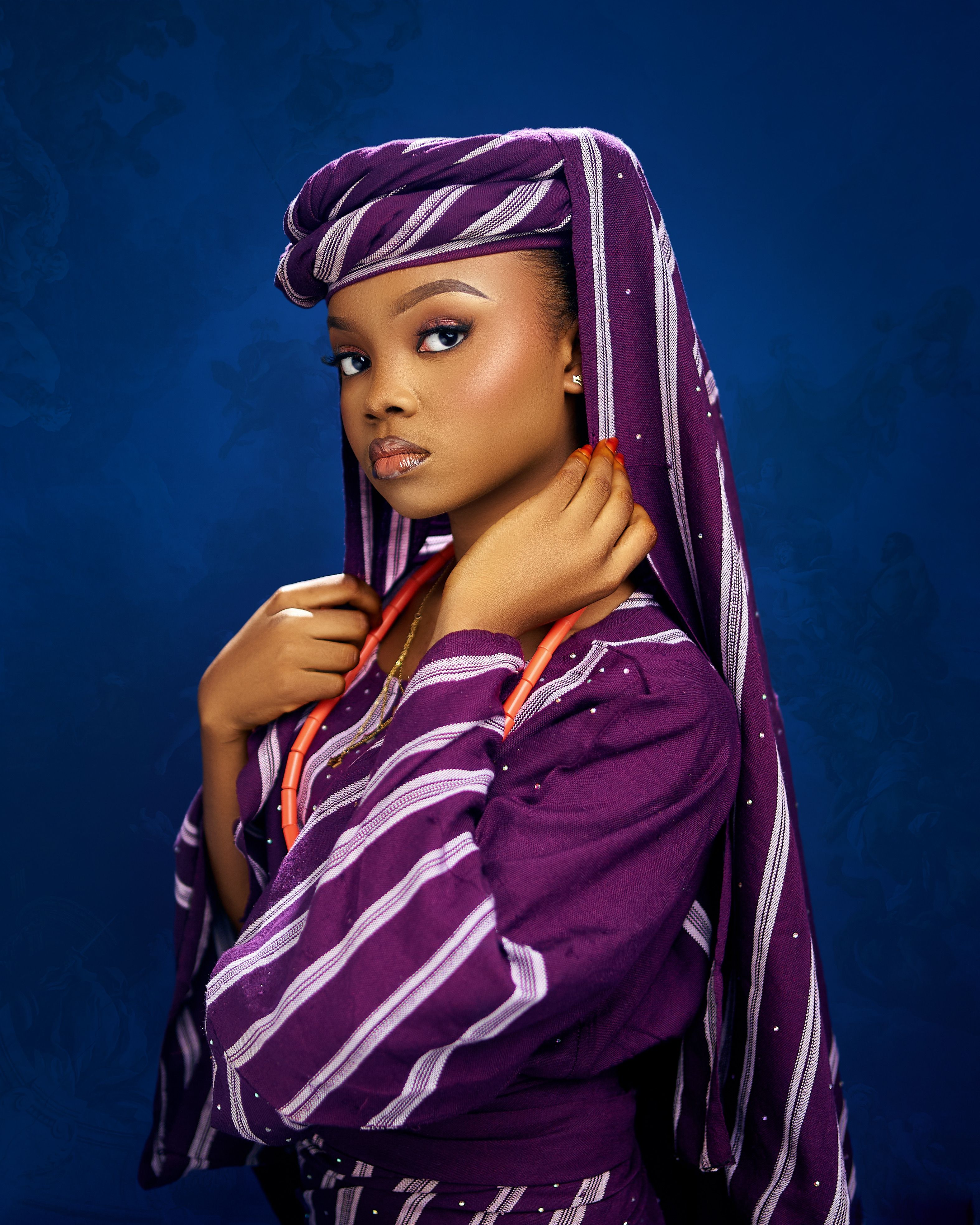 Portrait of a woman in purple African attire with headscarf, posing elegantly against a blue background.