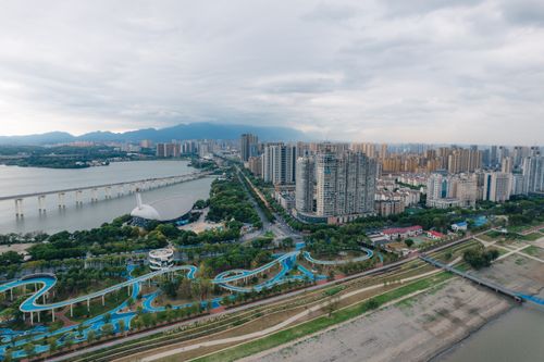Free Aerial cityscape of high-rise buildings, river, and lush greenery under a cloudy sky. Stock Photo