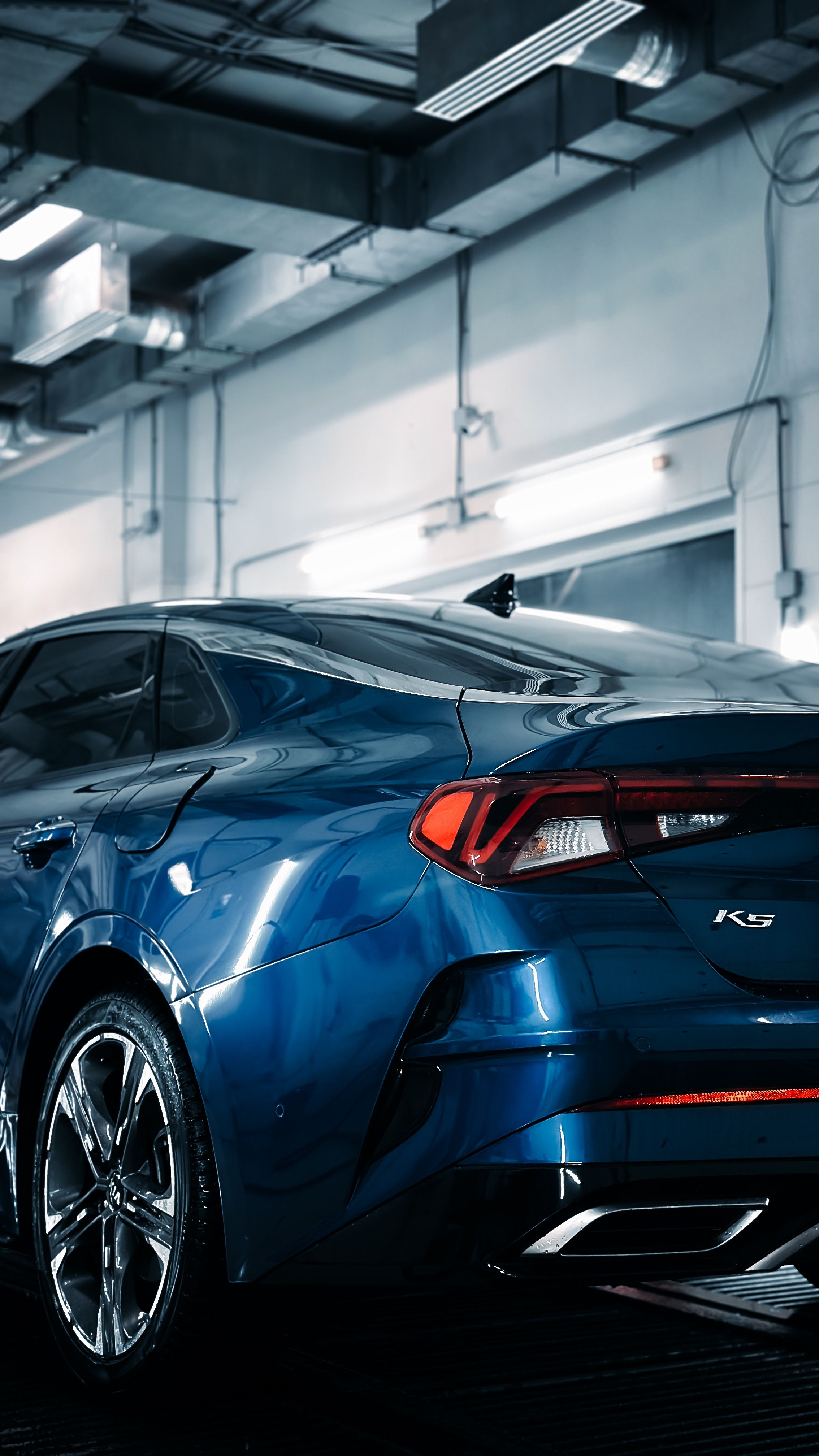 A stylish blue car with a polished finish parked in a modern indoor garage, highlighting its design.