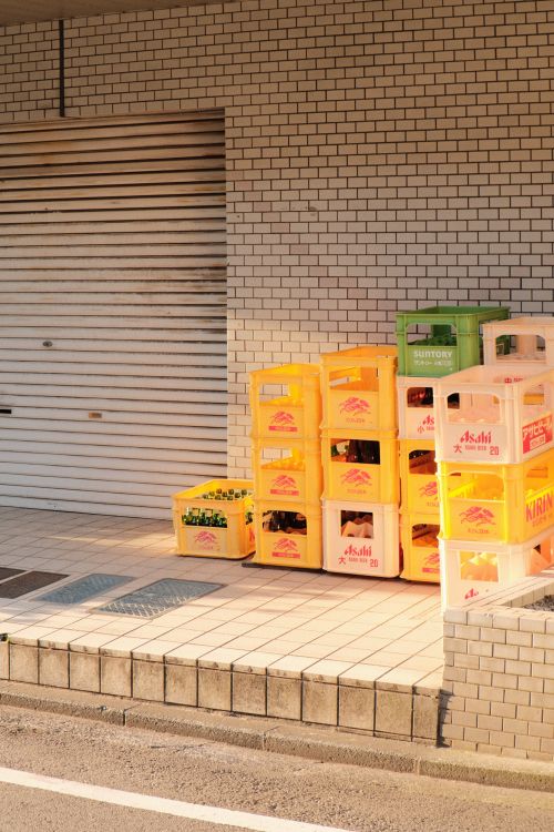Free Stacked beverage crates outside a building with a tiled wall on a sunny day. Stock Photo