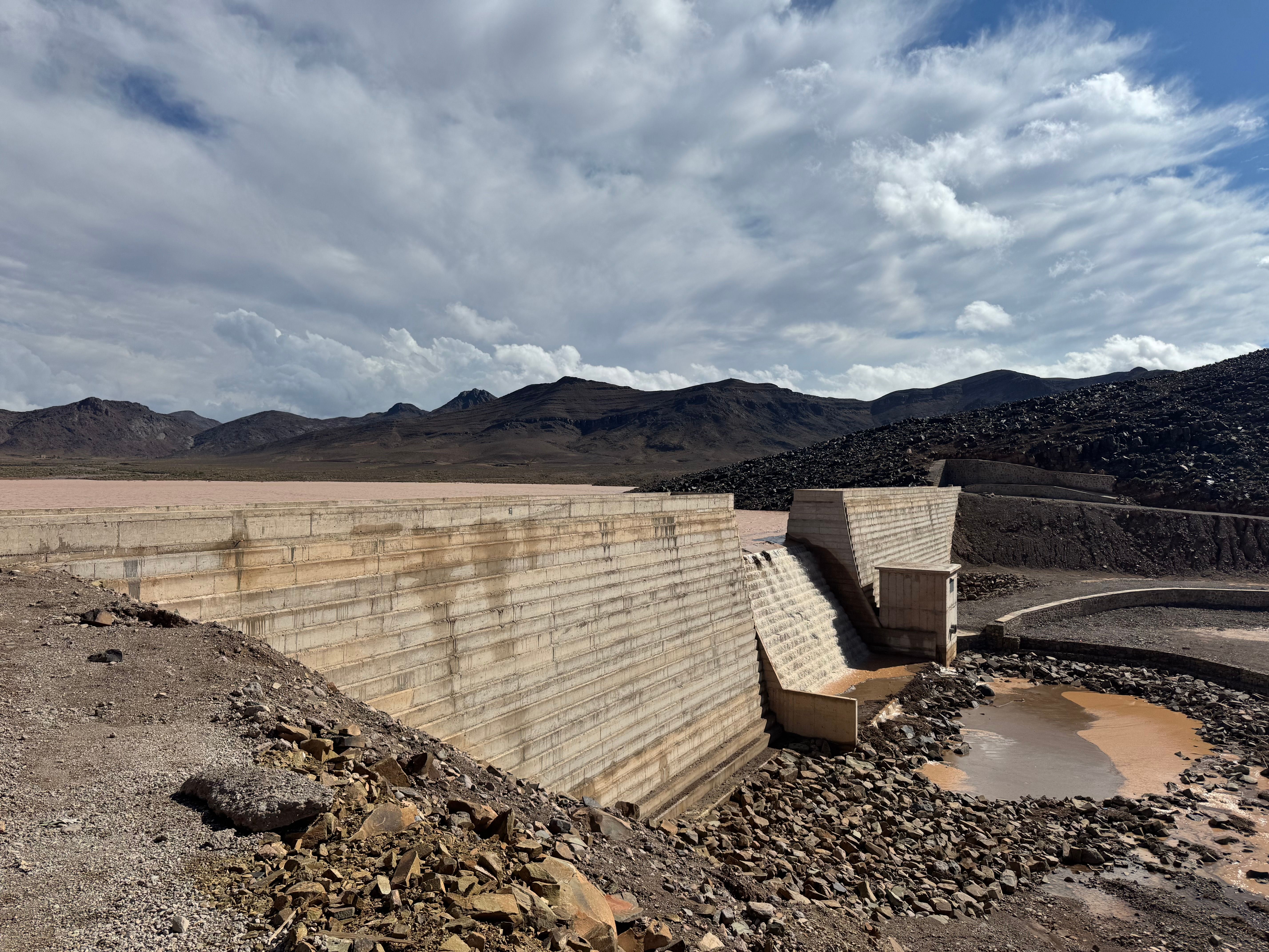 Stunning view of a concrete dam set against a mountainous and arid landscape, under a clear blue sky