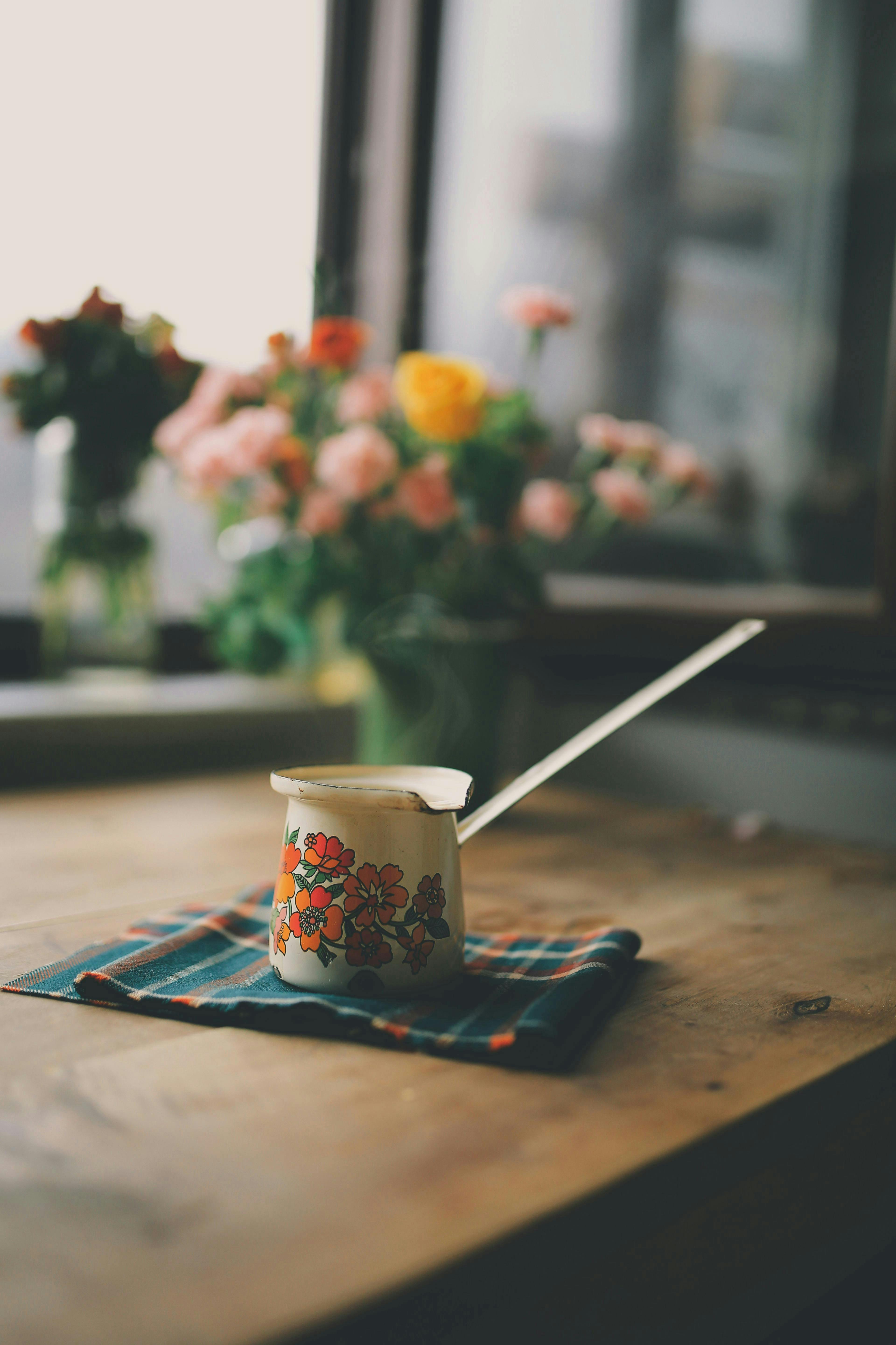 Charming vintage pot with floral design on a wooden table beside flowers.