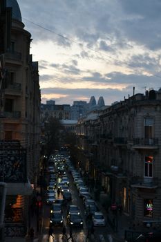 Evening traffic flows through a historic city street as dusk falls, capturing the urban hustle under a moody sky.