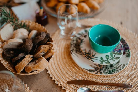 Cozy breakfast setup with various breads and ceramic tableware on a woven placemat.