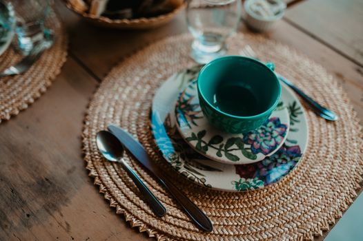 Beautiful rustic table setting featuring woven mats, floral plates, and teal cup.