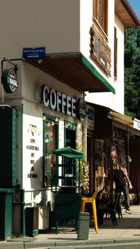 Quaint coffee shop exterior on a sunny street corner with people enjoying afternoon beverages.