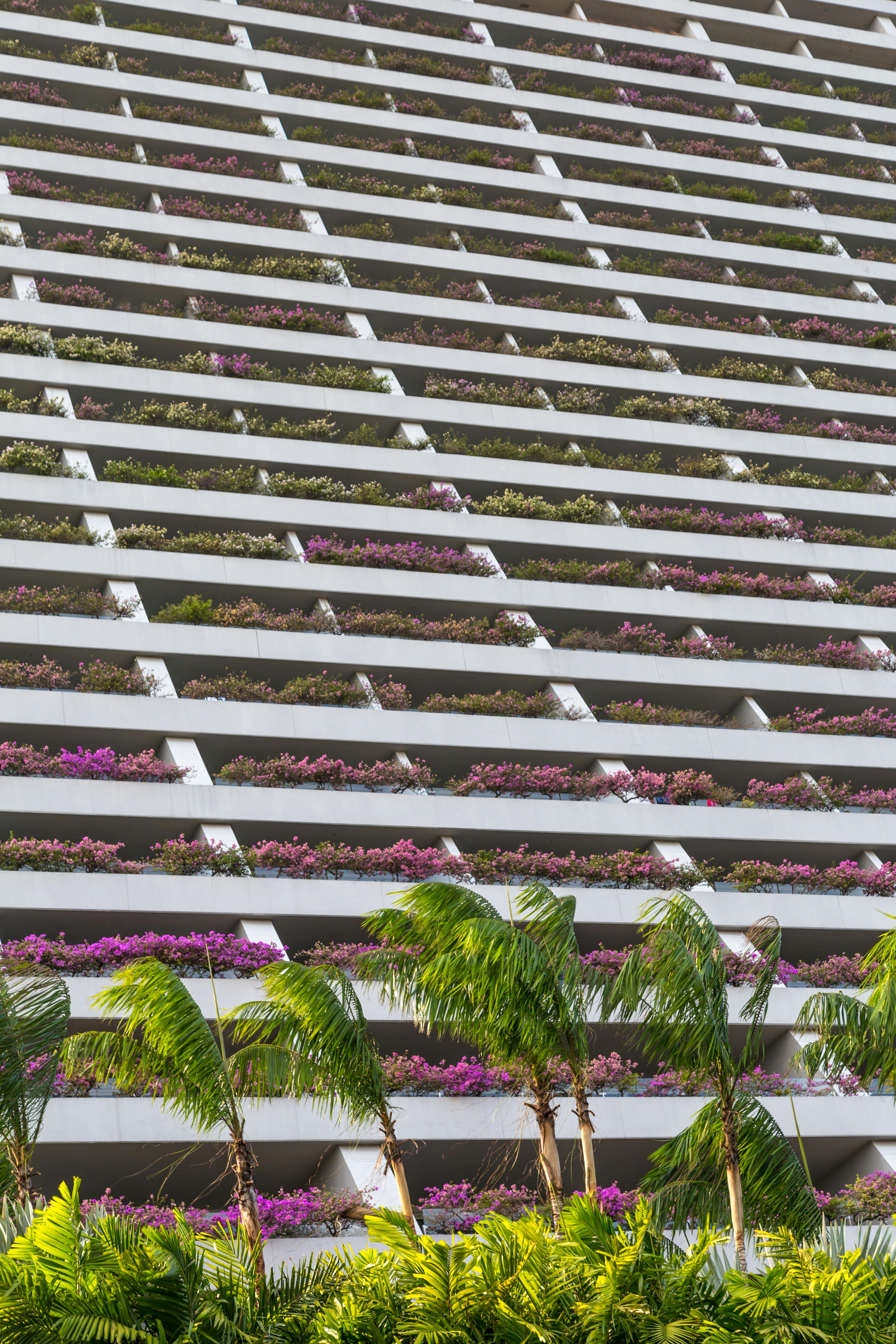 A modern building featuring vertical gardens and lush palm trees in an urban setting.