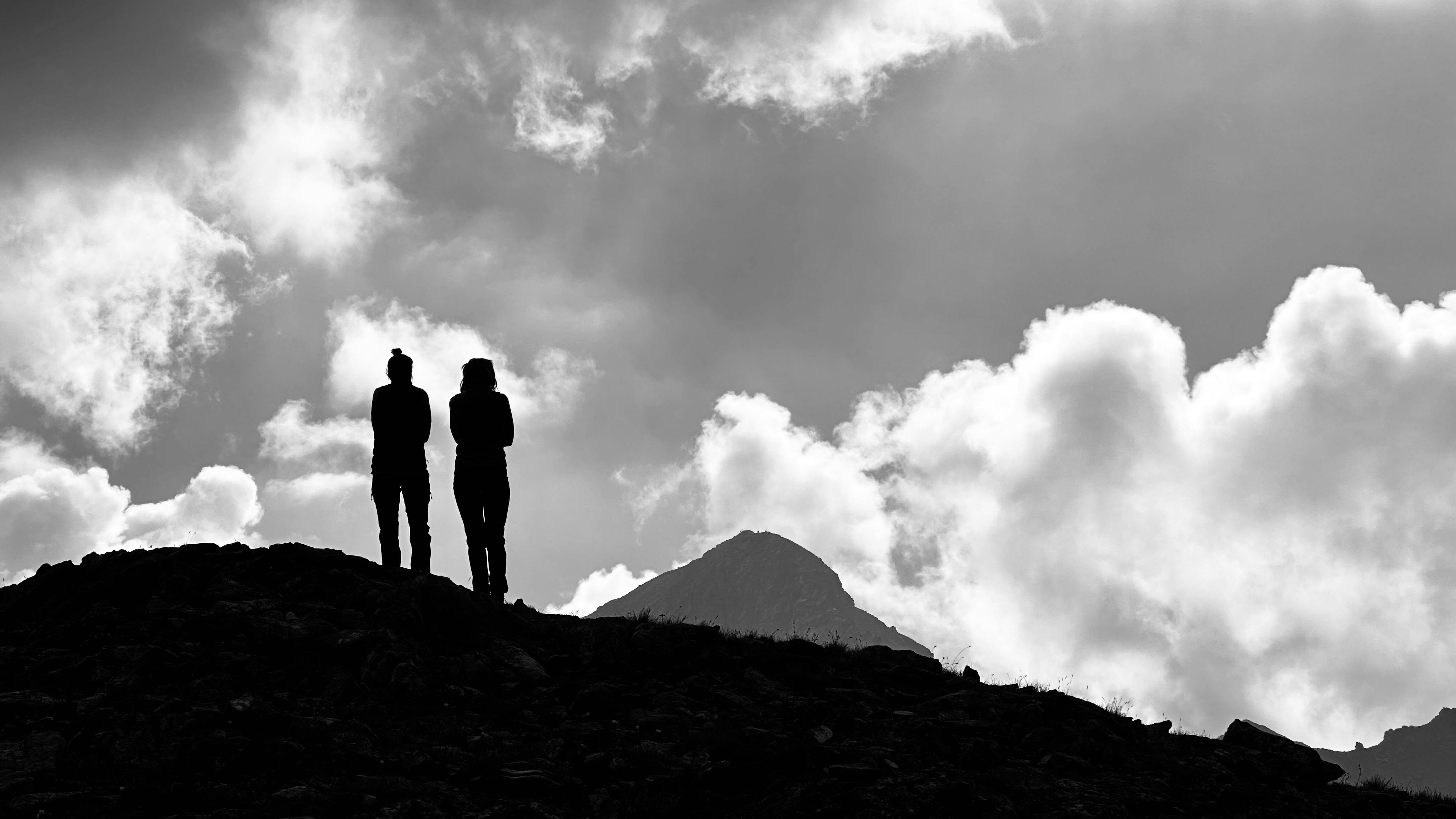 Silhouettes of people standing on a hill with mountains and clouds in Alagna Valsesia, Italy.