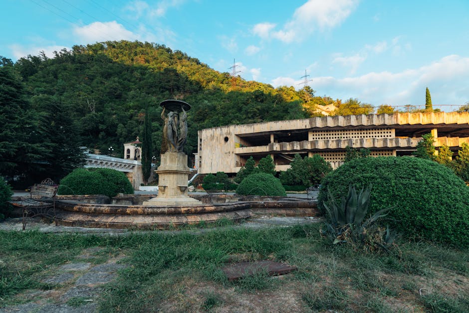 Abandoned building and stone fountain in Гагра, surrounded by lush greenery.