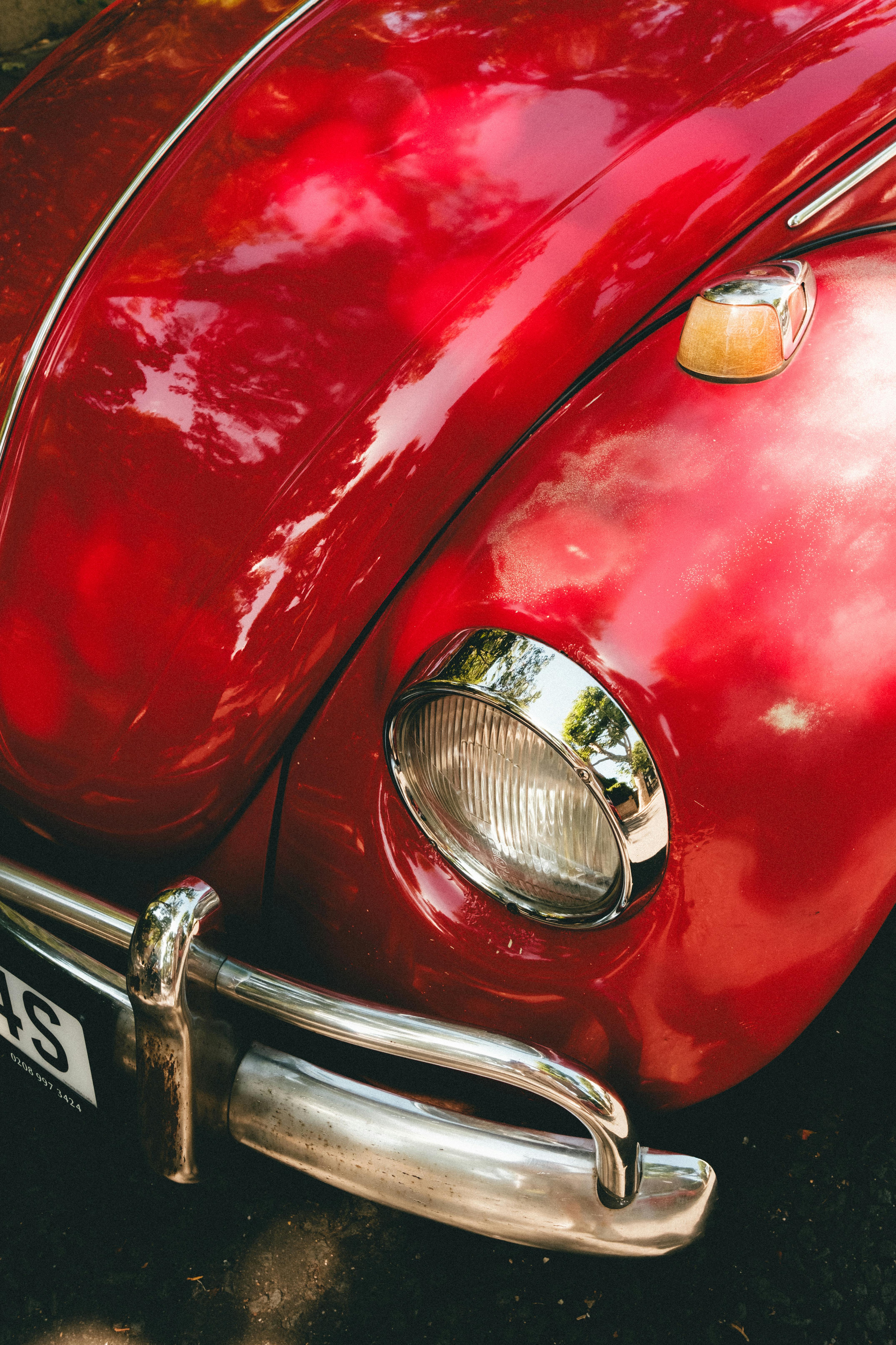 Close-up of a classic red Volkswagen Beetle, showcasing its shiny chrome details.