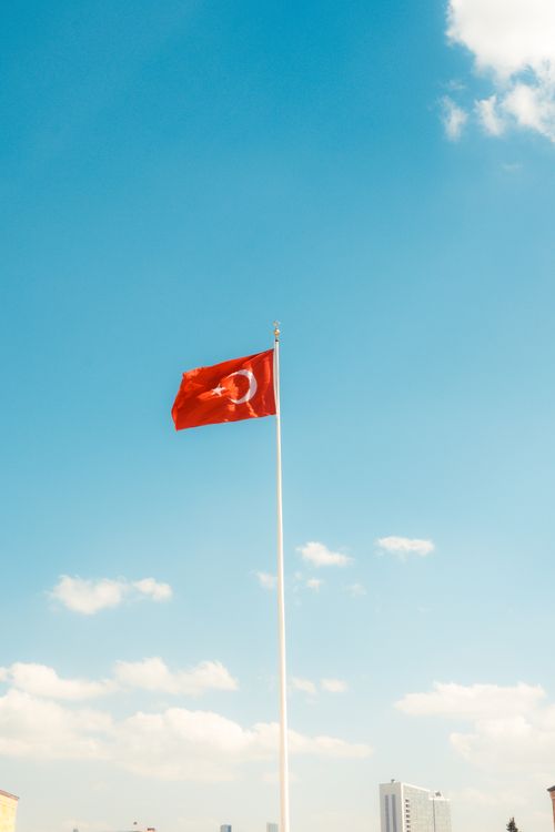 Free Turkish flag on tall pole waving against a clear blue sky with scattered clouds. Stock Photo
