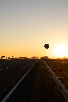 Peaceful sunrise over an empty highway with a silhouette of road signs in the distance.