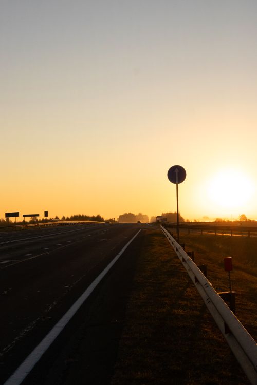 Free Peaceful sunrise over an empty highway with a silhouette of road signs in the distance. Stock Photo