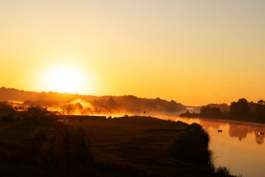 A beautiful sunrise illuminating a mist-covered river, creating a tranquil and warm atmosphere.
