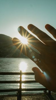 A hand silhouette capturing sunrays and reflections by a serene lake, evoking tranquility.