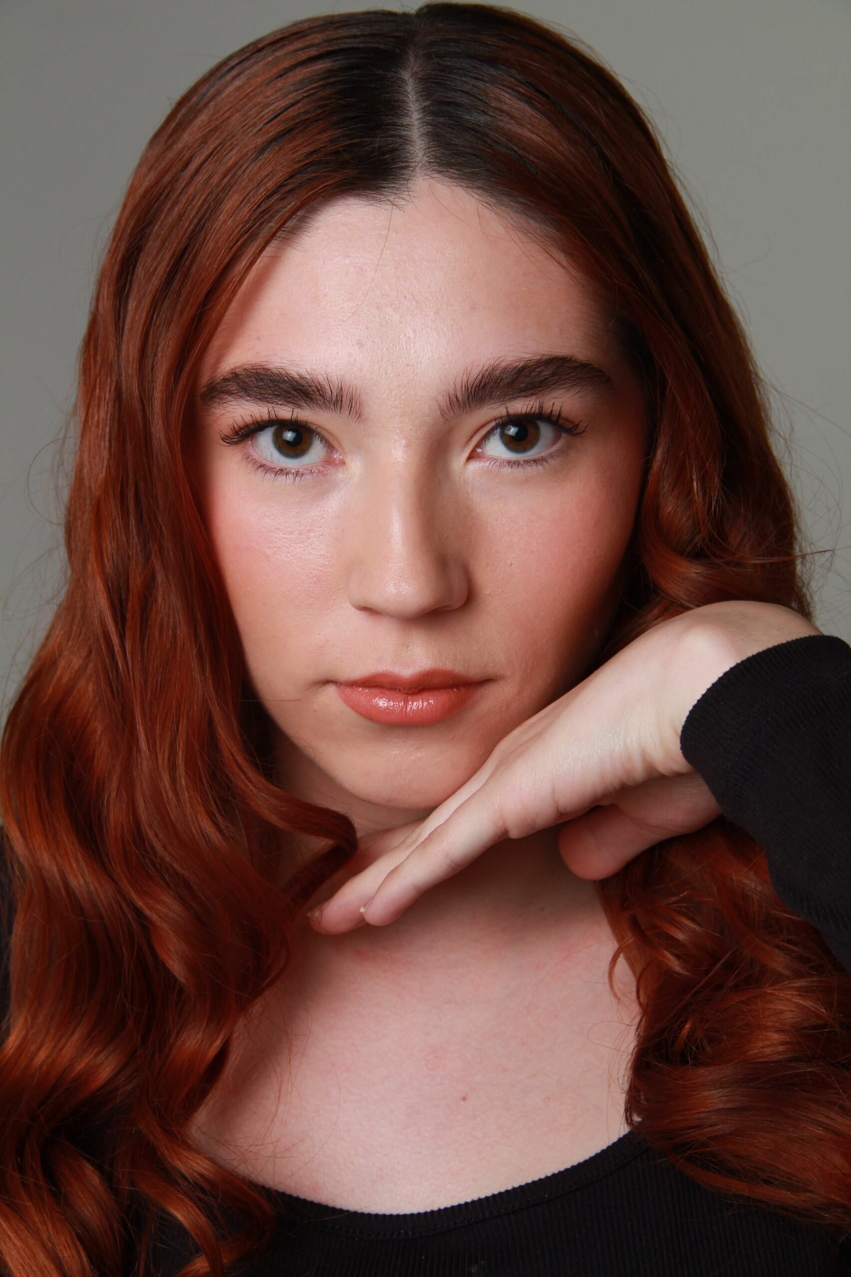 Close-up portrait of a young woman with auburn hair and soft lighting.