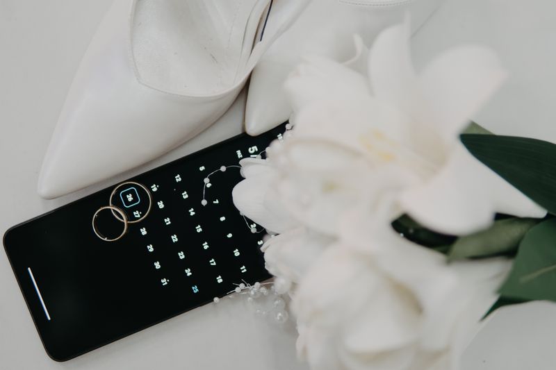 Flat lay of wedding essentials including high heels, rings, and a bouquet on a calendar.