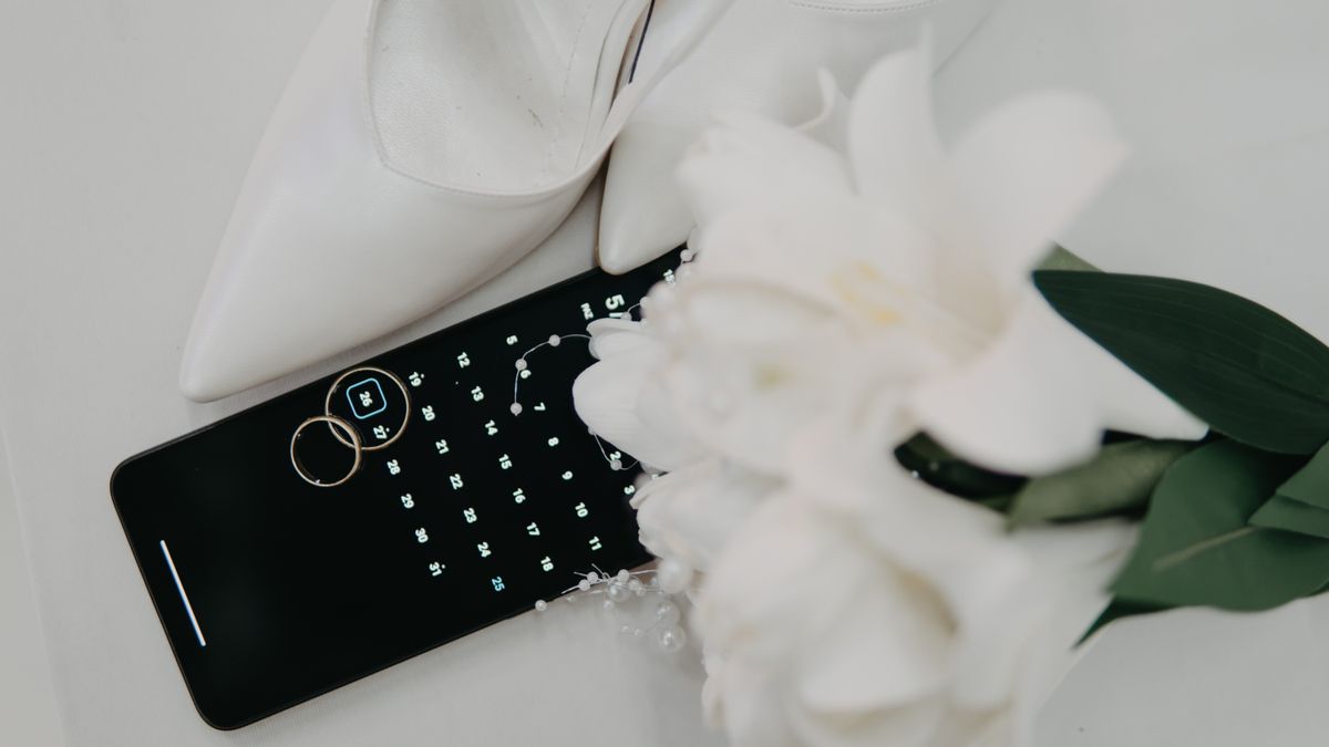 Elegant wedding-day essentials flat-lay: high heels, rings, bouquet, and a calendar app