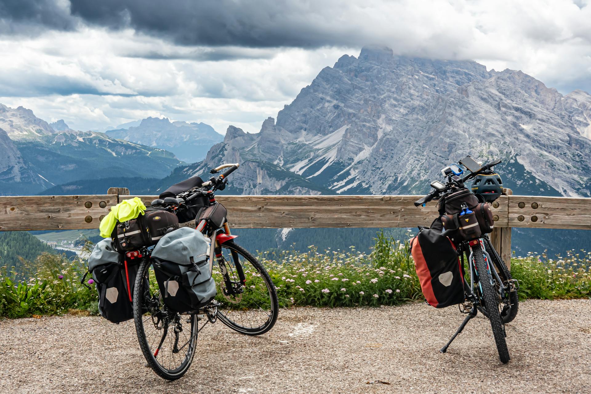 Two touring bicycles with luggage parked against a scenic mountain backdrop under cloudy skies.