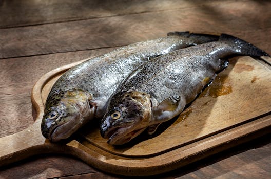 Two whole fresh rainbow trouts placed on a wooden cutting board, ready for cooking preparation.